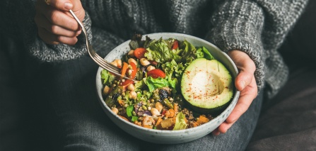 Closeup of a healthy salad held by a woman in a chunky gray sweater