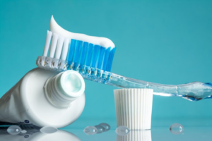 Toothbrush leaning against a tube of toothpaste on aqua blue background