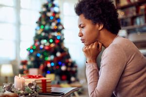 Concerned woman resting chin on jaw with Christmas tree in background